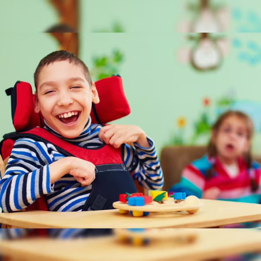 A smiling child at a wooden desk with colourful learning toys, supported in a bright, welcoming classroom